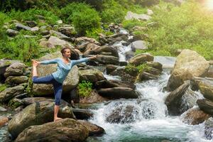 mujer haciendo yoga asana natarajasana al aire libre a cascada foto