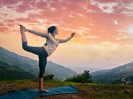 Woman doing yoga asana Natarajasana outdoors at waterfall photo