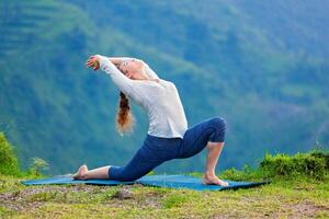 Sporty fit woman practices yoga asana Anjaneyasana in mountains photo
