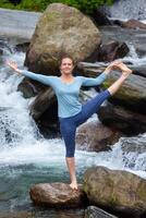 Woman doing Ashtanga Vinyasa Yoga asana outdoors at waterfall photo