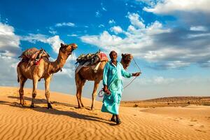 Cameleer camel driver with camels in dunes of Thar desert photo