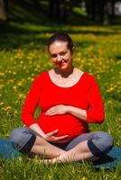 Pregnant woman doing asana Sukhasana outdoors photo