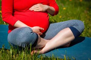 Pregnant woman doing asana Sukhasana outdoors photo