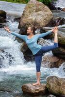 Woman doing yoga asana Natarajasana outdoors at waterfall photo