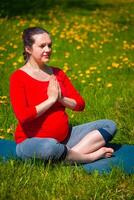 Pregnant woman doing asana Sukhasana outdoors photo