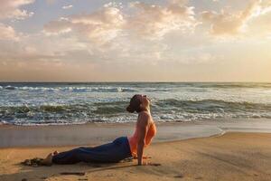 Woman practices yoga asana Urdhva Mukha Svanasana at the beach photo