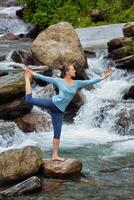 Woman doing yoga asana Natarajasana outdoors at waterfall photo
