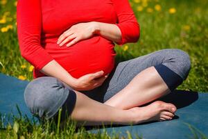 Pregnant woman doing asana Sukhasana outdoors photo