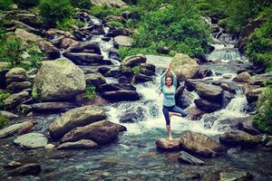 Woman in yoga asana Vrikshasana tree pose at waterfall outdoors photo