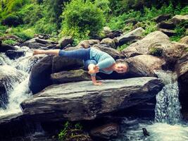 joven deportivo ajuste mujer haciendo yoga exteriores a tropical cascada foto