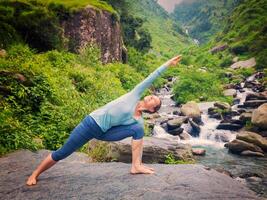 Woman practices yoga asana Utthita Parsvakonasana outdoors photo