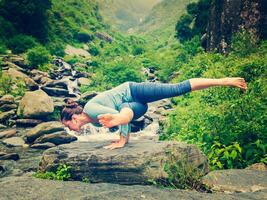 joven deportivo ajuste mujer haciendo yoga exteriores a tropical cascada foto