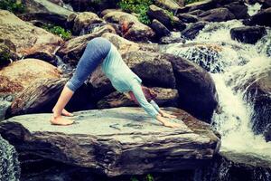 joven deportivo ajuste mujer haciendo yoga exteriores a tropical cascada foto