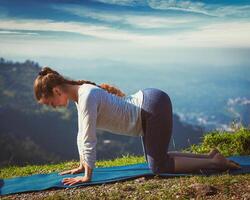 Sporty fit woman practices yoga asana bitilasana outdoors photo