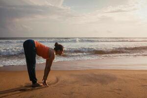 mujer haciendo yoga Dom saludo surya namaskar en playa foto