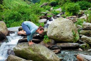 Woman doing Kakasana asana arm balance outdoors photo