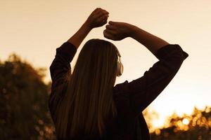 silueta de joven mujer en auriculares disfrutando música y bailando a puesta de sol foto