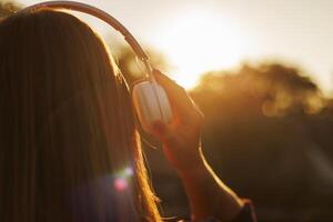 joven mujer en auriculares escuchando a música a puesta de sol foto