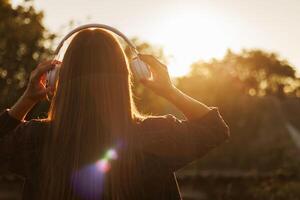 joven mujer en auriculares escuchando a música a puesta de sol foto