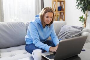 Woman working on a laptop sitting at a table on the couch at home photo