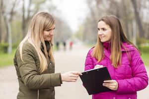 Two women engaged in a conversation with a clipboard on a park path photo