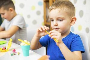 linda niños sentado a el mesa y obras de teatro con plastilina foto