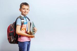 School boy with backpack holding books on blue background for education concept photo