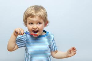 Little blonde boy brushing teeth with toothbrush on blue background photo