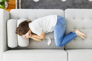 Frustrated woman covering face and crying, lying on sofa at home alone photo