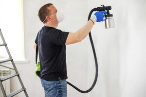 Worker in protective mask painting wall with spray gun photo