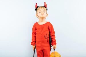 Happy cheerful boy in devil costume with trident on blue background photo