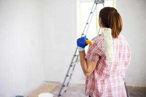 Positive satisfied woman holding dirty roller after painting walls in room photo