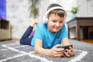 A child boy with phone and headphones is lying on the floor photo
