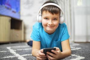 A child boy with phone and headphones is lying on the floor photo