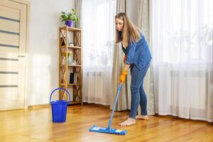 A young woman washes the floor with a mop in the living room photo