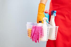 mujer en guantes y delantal participación cesta con esponja y limpieza productos foto