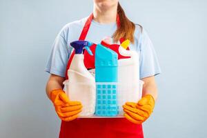 mujer en guantes y delantal participación cesta con esponja y limpieza productos foto