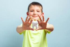 Child shows big white toy tooth on a blue background. Caring for teeth photo