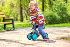 Active blond boy riding balance bike or run bike outdoor park photo