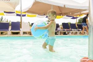 niño nadar, bucear, ocio y jugando inflable pelota en piscina a vacaciones foto