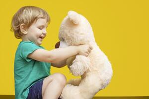 Little boy hugging teddy bear toy on yellow background photo