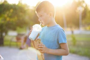 A child drinks a milkshake and eats a hotdog outdoors in a park photo