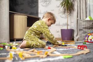 Baby playing with toy railroad, trains and cars on the floor photo