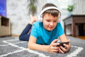 A child boy with phone and headphones is lying on the floor photo