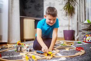 Boy playing with toy train with wooden rails while sitting on floor at home photo