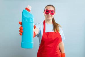 joven mujer en rojo mascarilla, caucho guantes y delantal participación detergente botella foto