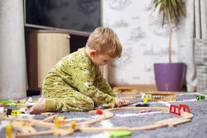 Baby playing with toy railroad, trains and cars on the floor photo