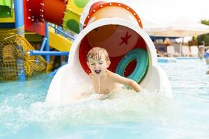 pequeño chico jugando en agua diapositiva en al aire libre piscina en un caliente verano día foto