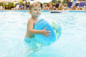 niño nadar, bucear, ocio y jugando inflable pelota en piscina a vacaciones foto