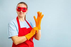 Young woman in red mask and apron puts on rubber gloves on blue background photo